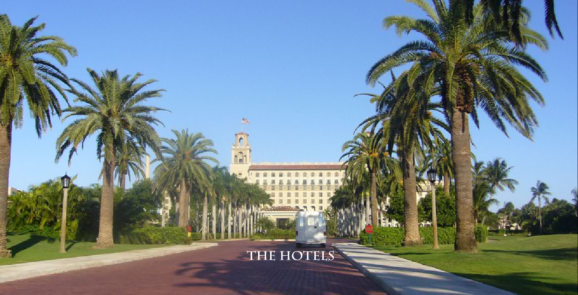 A hotel with palm trees and a clock tower in the background.
